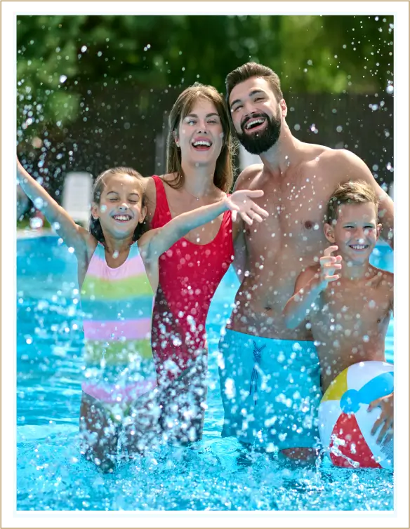 A happy family of four playing in a pool splashing water.